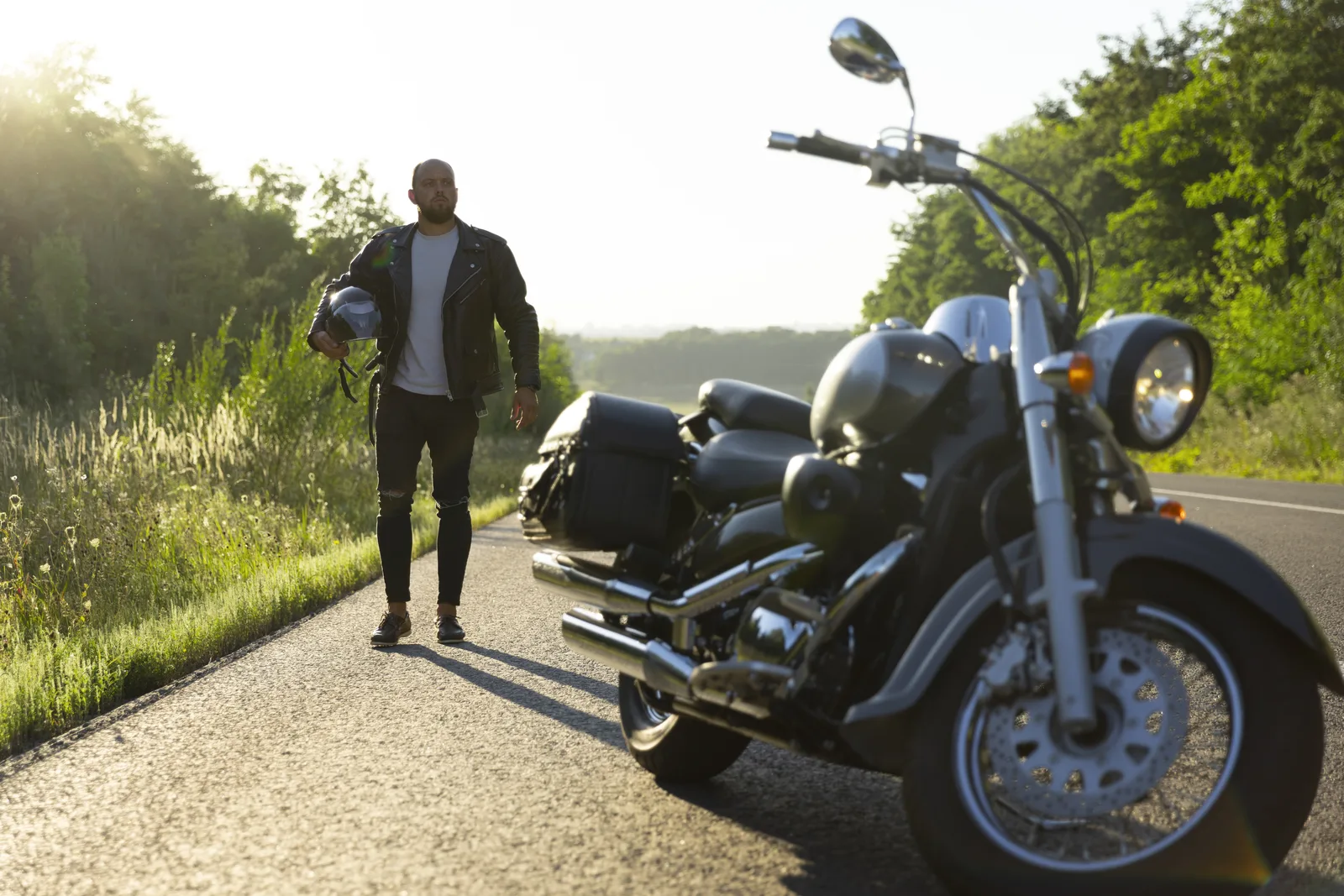 Rider walking back to a motorcycle stopped on a rural shoulder.
